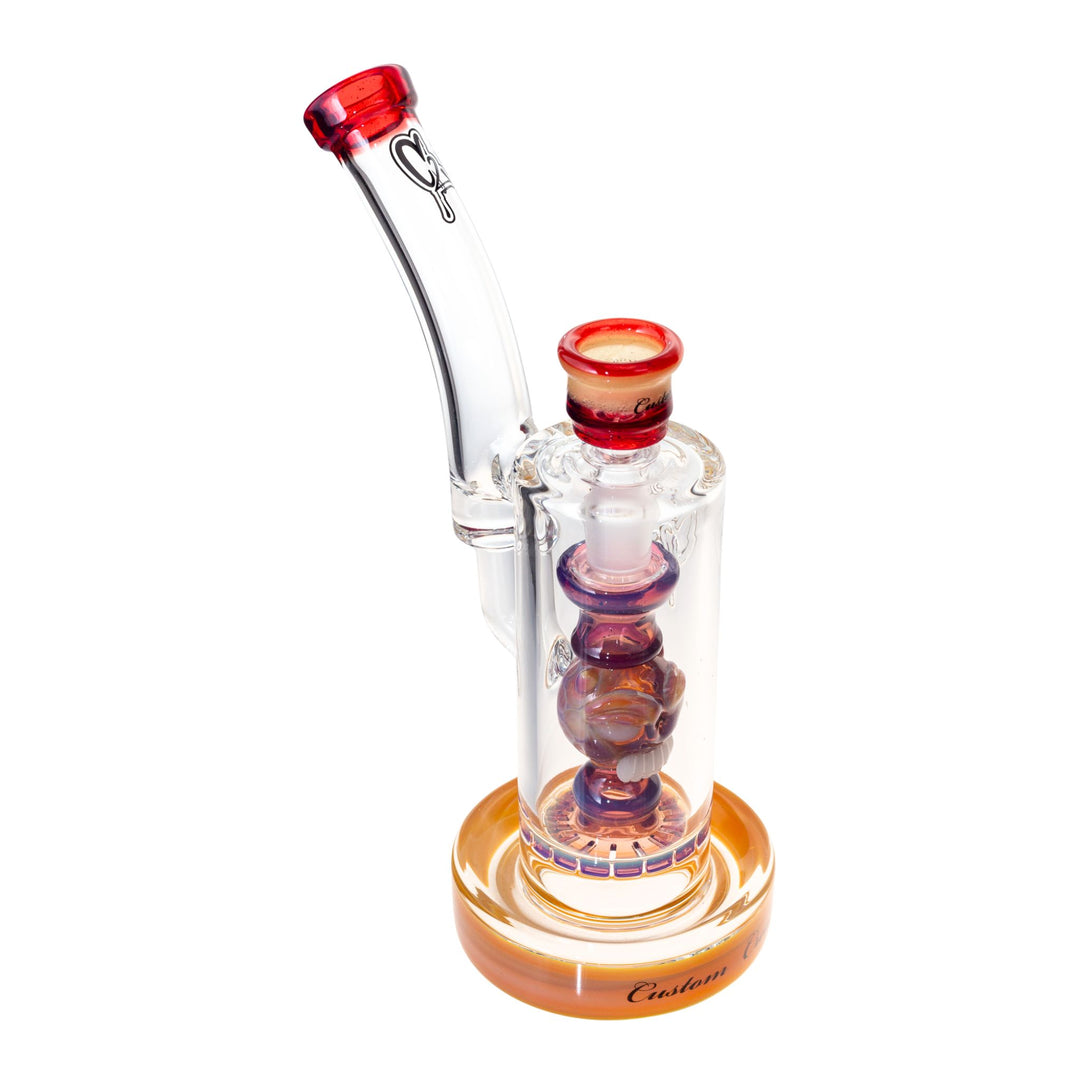 Side right view of a C2 50mm Bubbler. This piece features a ratchet filter, an ornate down stem, and a recessive joint. The colors are hues of orange, purple, and red. - Up N Smoke.