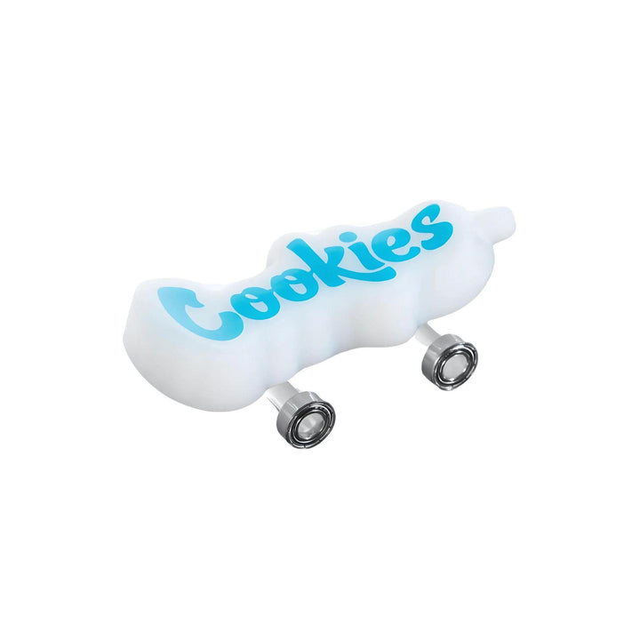 "A side photograph of the Cookies Toke Deck in a milky opaque white. The Cookies lettering is a light blue and on the top of the design. This hand pipe is modeled after a skateboard, and features mobile wheels. It is 4.25'', with the bowl on the underneath. Each Toke Deck comes with a two-piece grinder from Santa Cruz Shredder." - Up N Smoke.