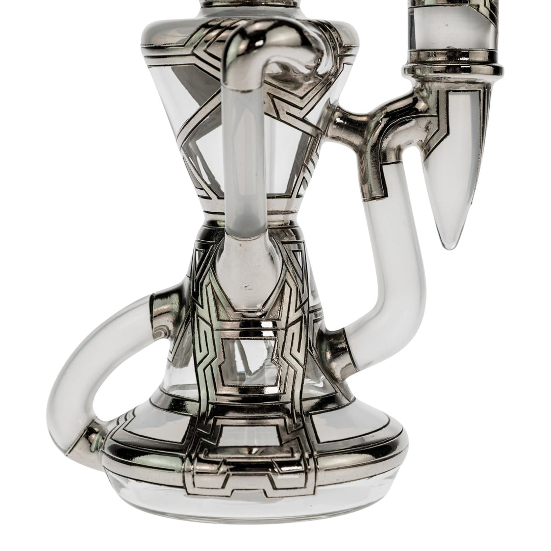 "Close-up of the base of a Ryan Fitt Klein Recycler that has a frosted bodice with silver geometric accents on a white background," - Up N Smoke.