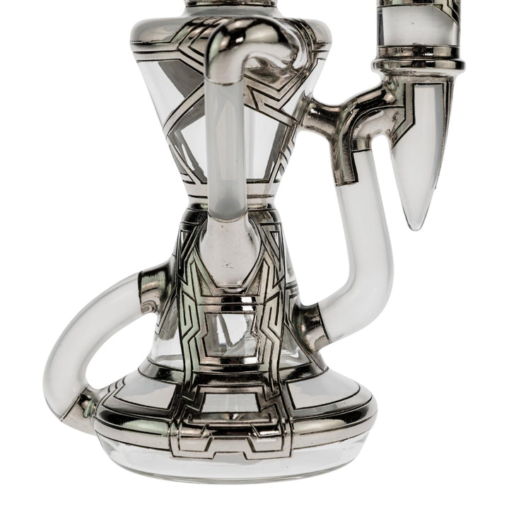 "Close-up of the base of a Ryan Fitt Klein Recycler that has a frosted bodice with silver geometric accents on a white background," - Up N Smoke.